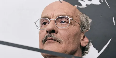 Portrait d'un homme avec des lunettes et une moustache partielle, visage sérieux.
