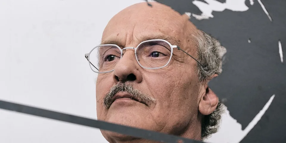 Portrait d'un homme avec des lunettes et une moustache partielle, visage sérieux.