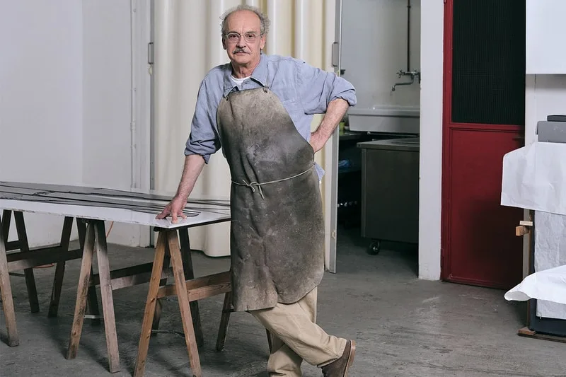 Homme avec tablier dans atelier, appuyé sur table.