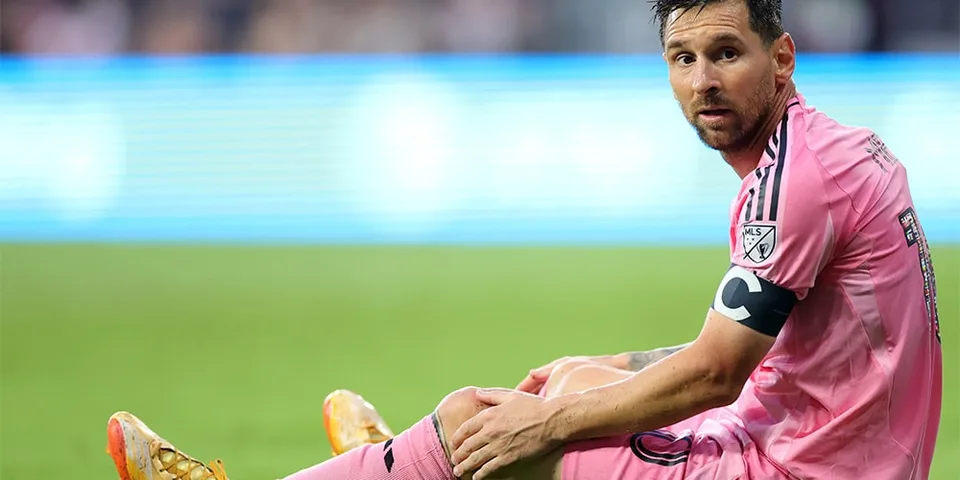 Joueur de football en uniforme rose assis sur le terrain lors d'un match.
