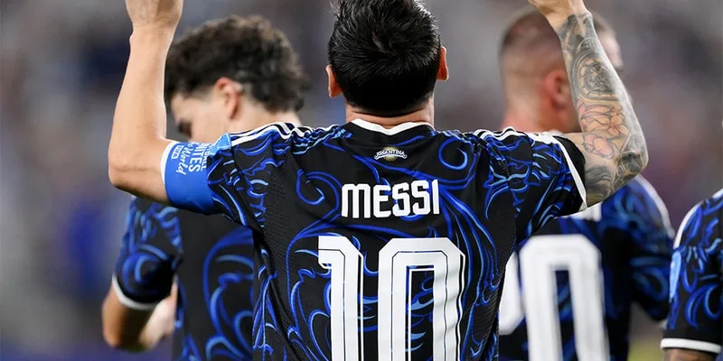 Joueur de football en maillot bleu et noir, numéro 10, lève les bras sur le terrain.