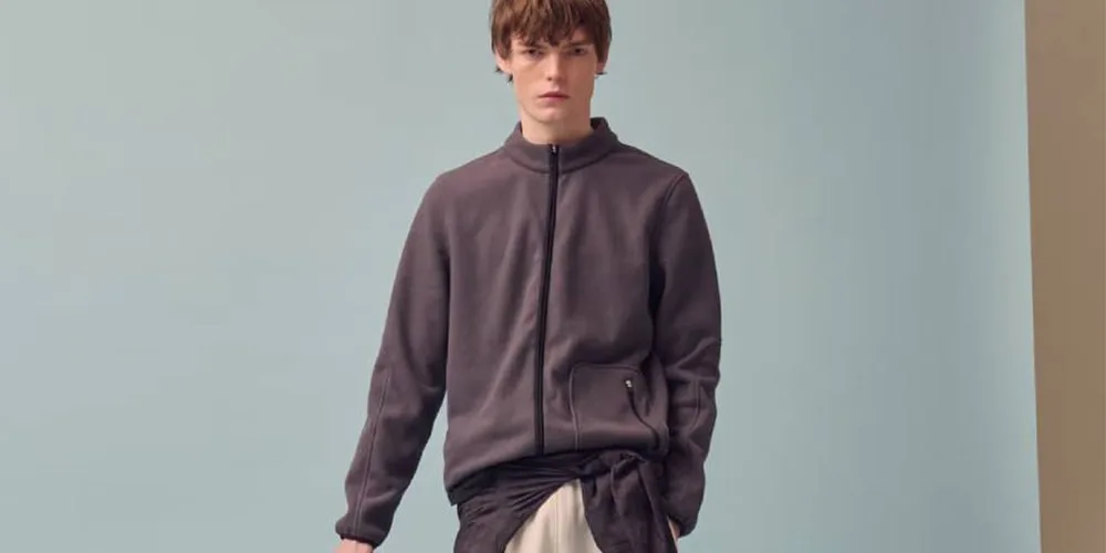 Homme en pull gris avec fond bleu, posant debout.