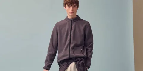 Homme en pull gris avec fond bleu, posant debout.