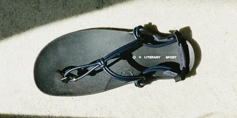 Sandale noire avec texte 'LITERARY SPORT' vu de dessus sur un sol ensoleillé.