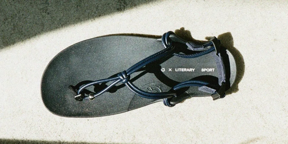 Sandale noire avec texte 'LITERARY SPORT' vu de dessus sur un sol ensoleillé.