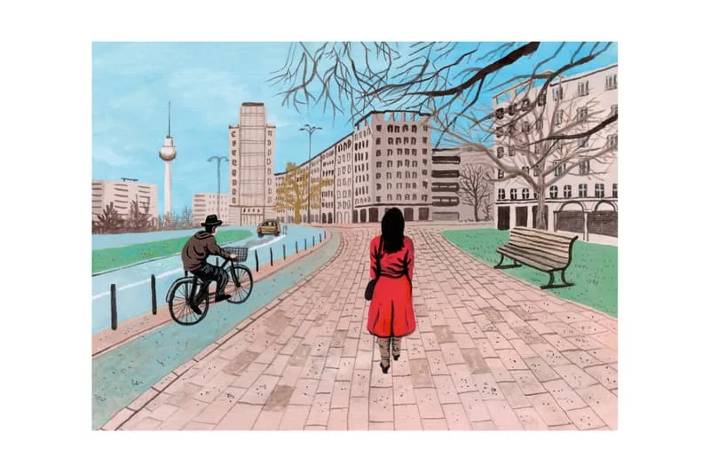 Femme en rouge sur chemin pavé, cycliste et bâtiments en arrière-plan.