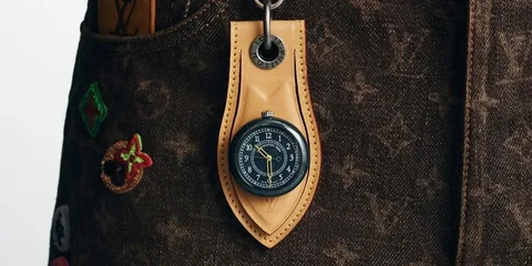 Sac à motif avec montre accrochée, fond brun et ornements colorés.