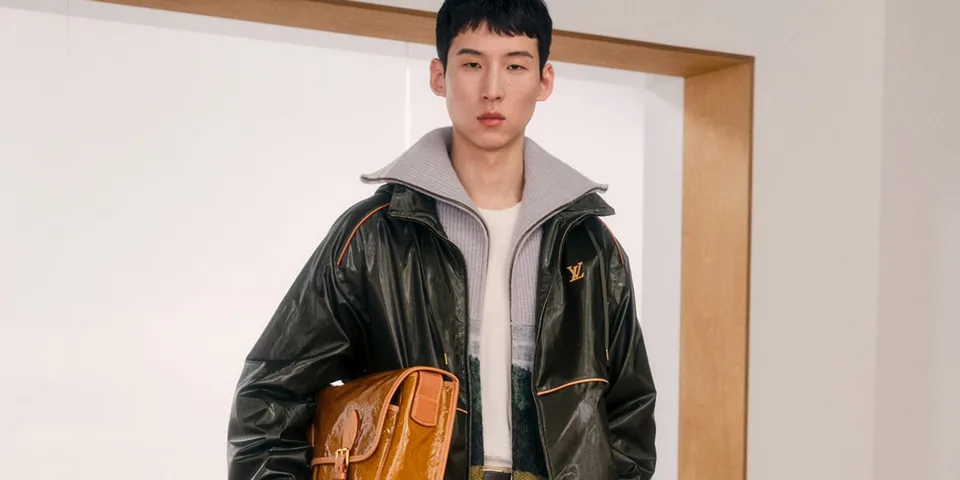Homme avec veste noire et sac marron, intérieur moderne