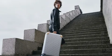 Personne portant une valise sur des escaliers en béton, ciel nuageux