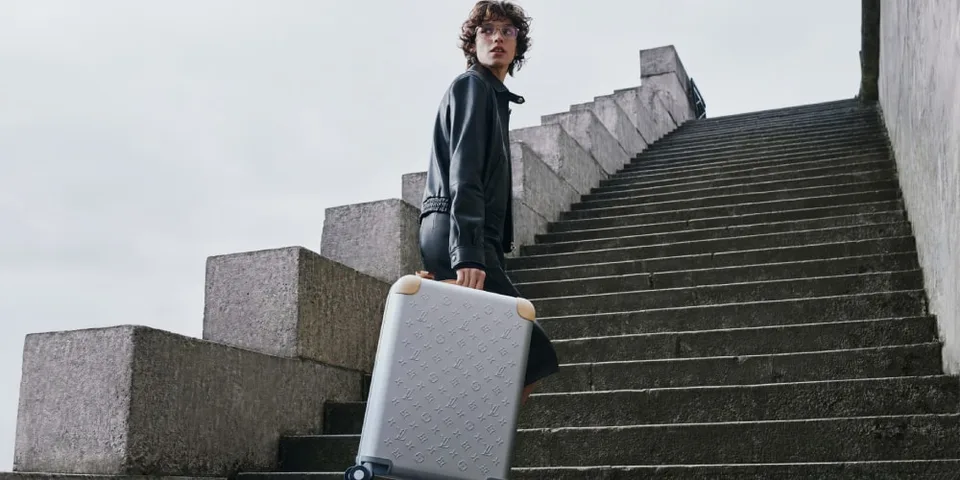 Personne portant une valise sur des escaliers en béton, ciel nuageux