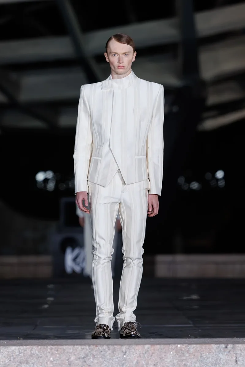 Homme en costume blanc défilant sur un podium.