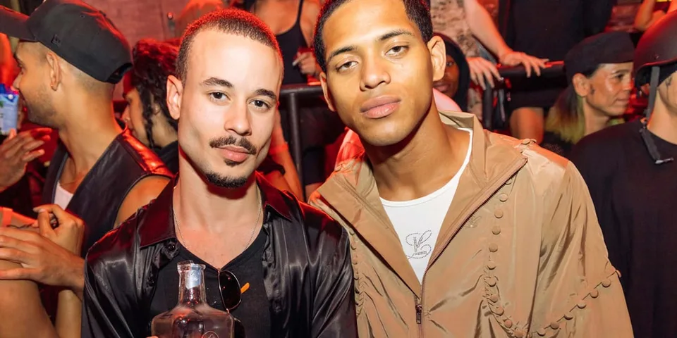 Deux hommes posent dans une foule animée lors d'une soirée.