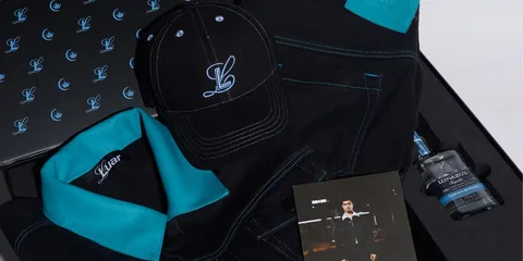 Vêtements noirs avec broderies bleu clair, casquette et bouteille de parfum.