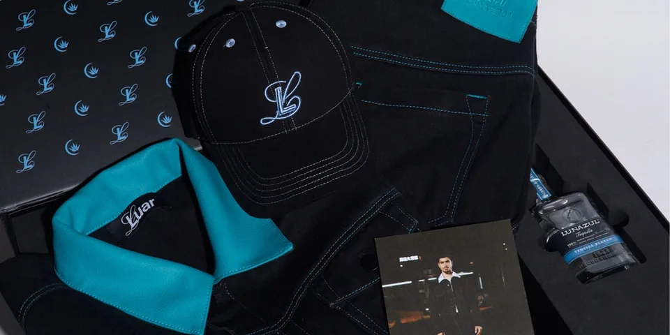 Vêtements noirs avec broderies bleu clair, casquette et bouteille de parfum.