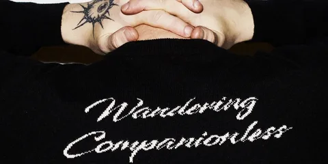 Dos tatoué avec pull "Wandering Companionless" visible.