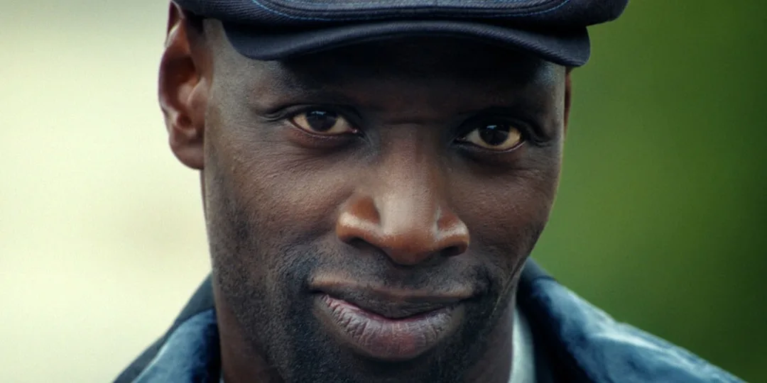 Homme souriant portant une casquette noire, fond flou.