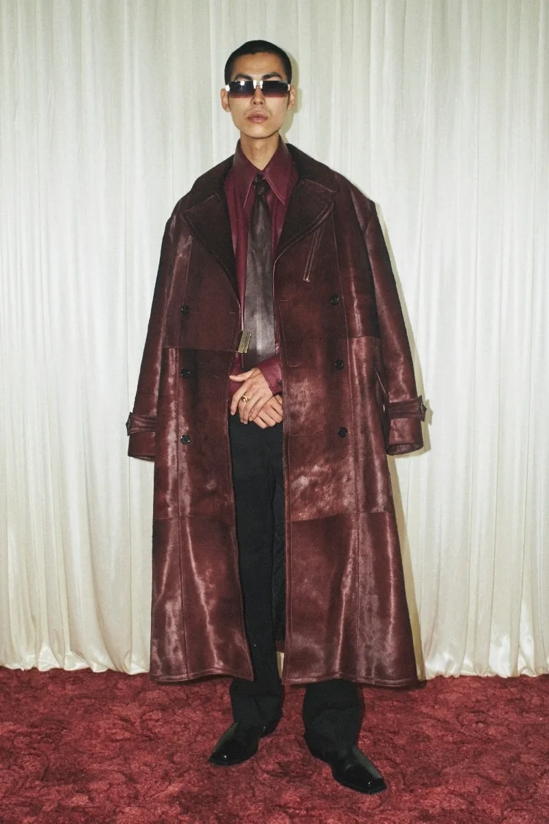 Homme en manteau long marron foncé, cravate et lunettes de soleil.