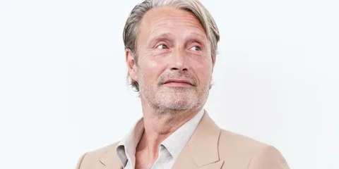 Homme en blazer beige, regard pensif sur fond clair.