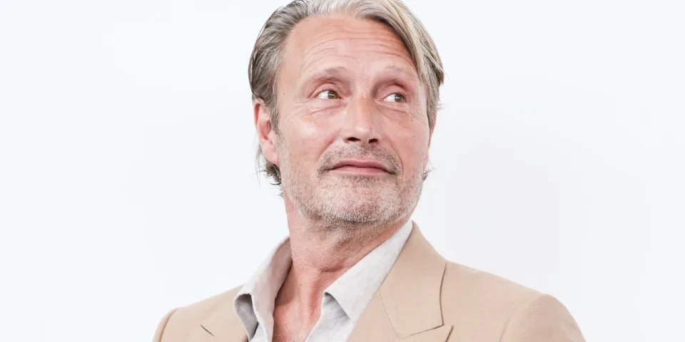 Homme en blazer beige, regard pensif sur fond clair.