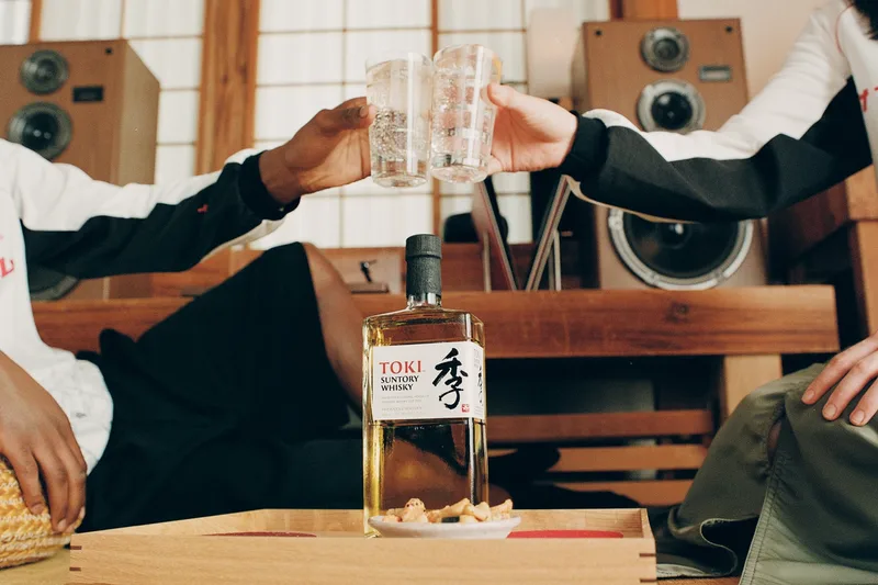 Deux personnes trinquent avec un whisky Toki sur une table.