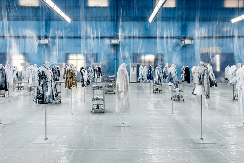 Exposition de manteaux suspendus dans une pièce bleue et transparente.