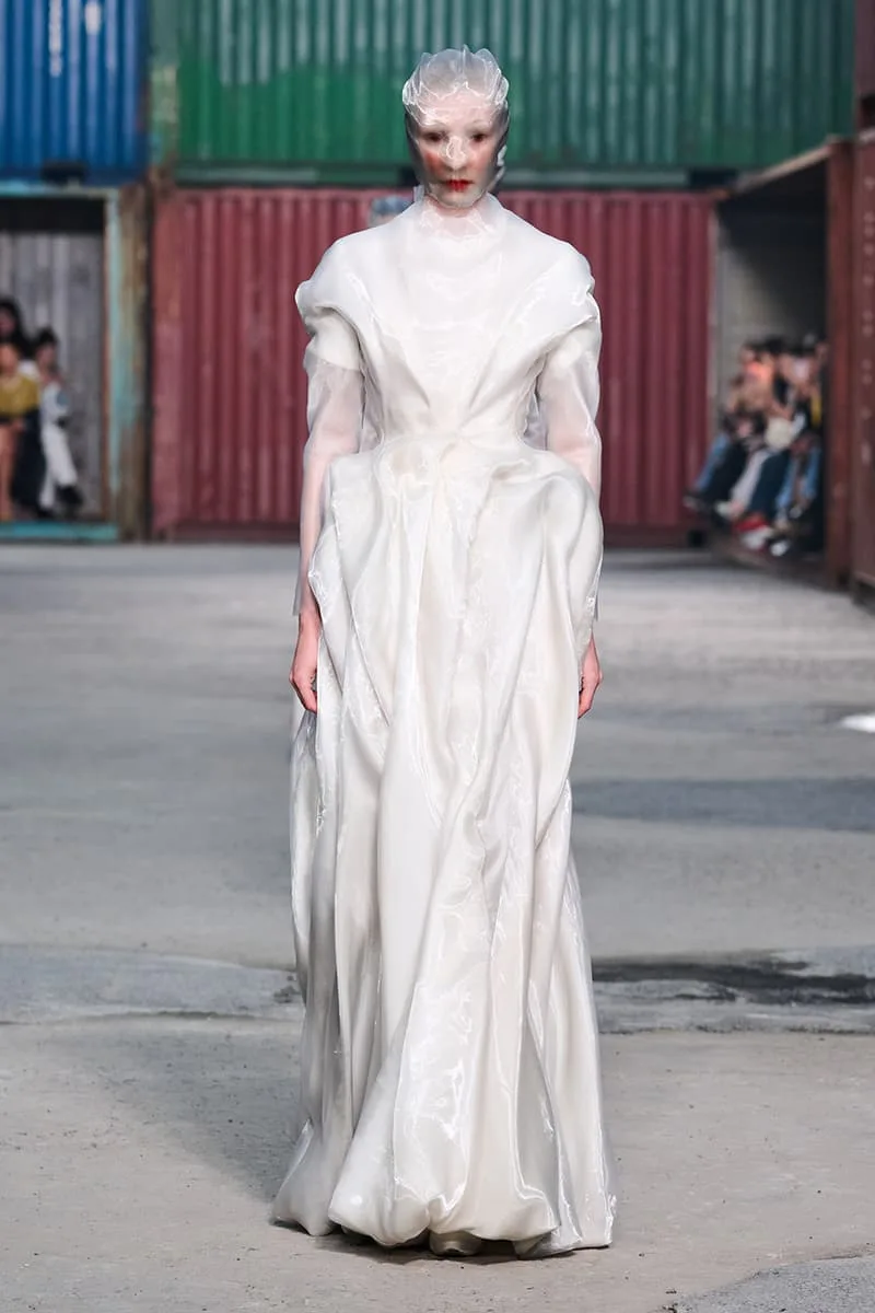 Mannequin défile en robe blanche vaporeuse sur un podium industriel.