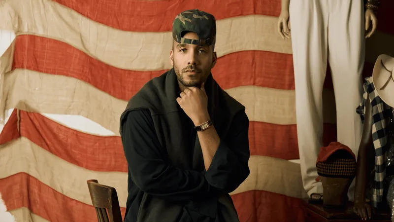 Homme avec casquette devant un drapeau, vêtements vintage autour.