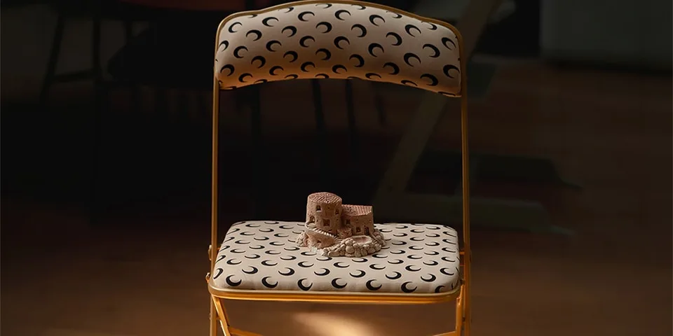 Chaise pliante avec motif croissant et château en sable en miniature.