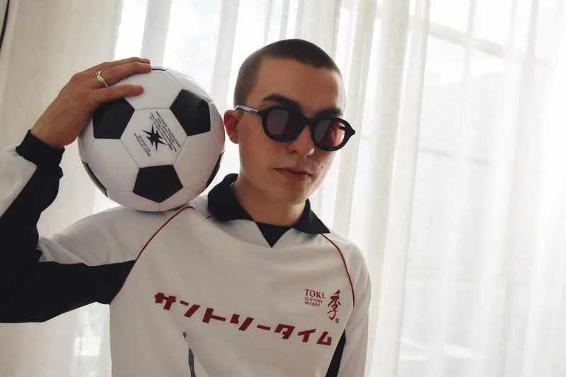Homme avec un ballon de foot sur l'épaule, portant des lunettes de soleil.