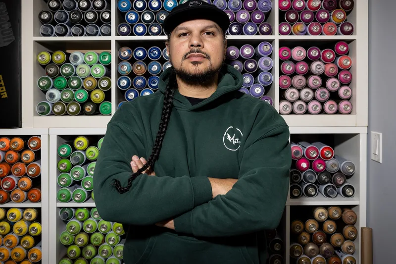 Homme avec tresse devant des étagères de bombes de peinture colorées.