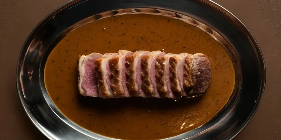Tranches de viande sur une sauce brune, servies sur un plat en métal argenté.