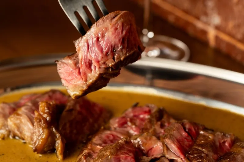 Un morceau de steak saignant sur une fourchette avec sauce.