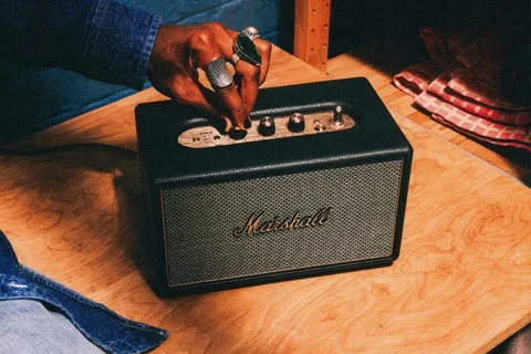 Haut-parleur noir Marshall sur table, main ajustant le bouton