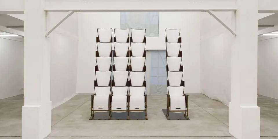 Sculpture de chaises blanches empilées en colonne dans une galerie.