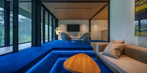 Salon moderne avec moquette bleue, canapé, table en bois et chaises.