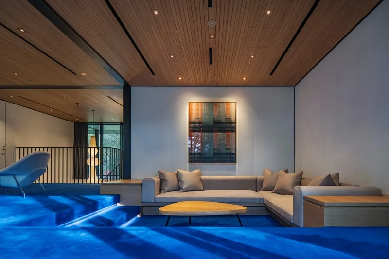 Salon moderne avec tapis bleu et canapé beige, mur décoré.