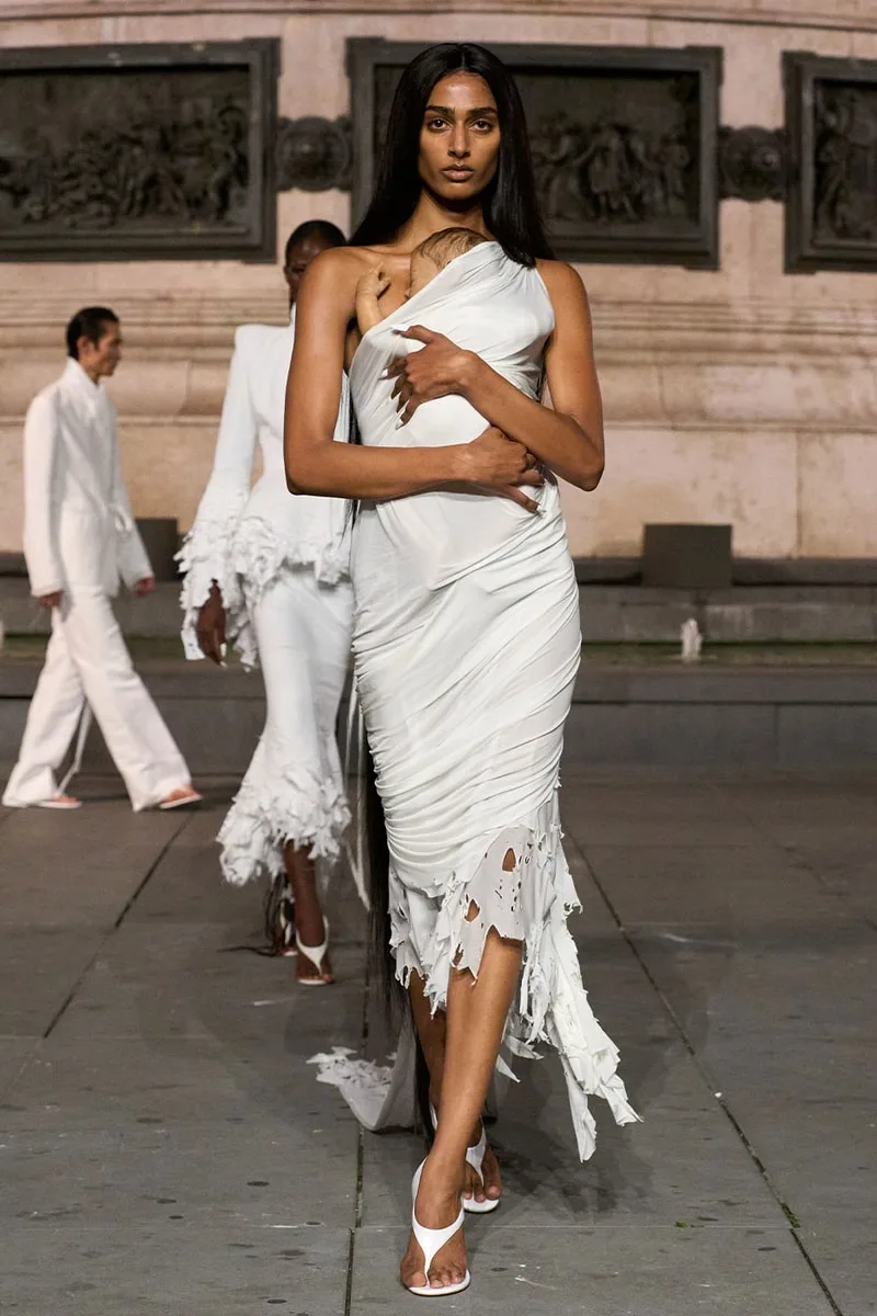 Modèle en robe blanche en marchant sur un podium en extérieur.