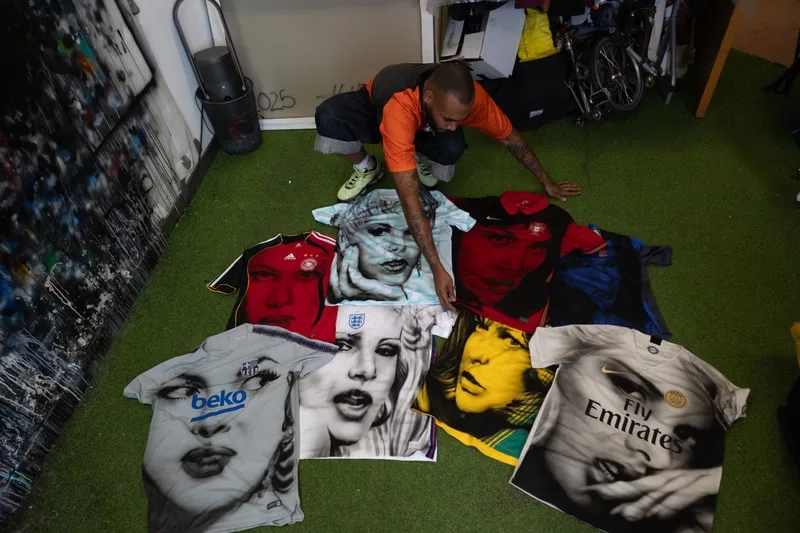 Homme posant avec des maillots de football artistiques au sol.