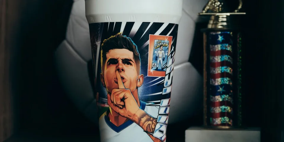 Gobelet avec dessin d'un joueur de football, ballon et trophée en arrière-plan.