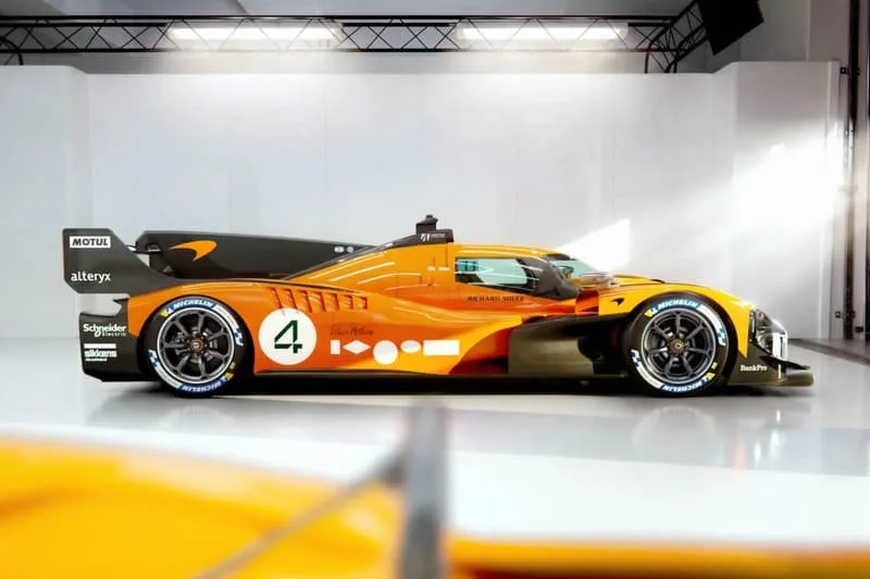 Voiture de course orange et noire exposée dans un studio lumineux.
