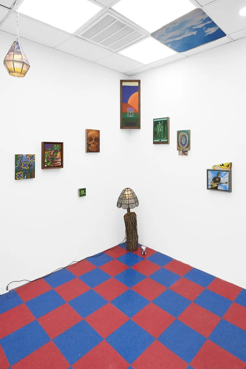 Salle d'exposition avec œuvres et sol quadrillé rouge et bleu.
