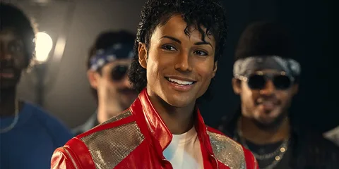 Personne en veste rouge brillante, cheveux bouclés, souriant, entourée par d'autres personnes.