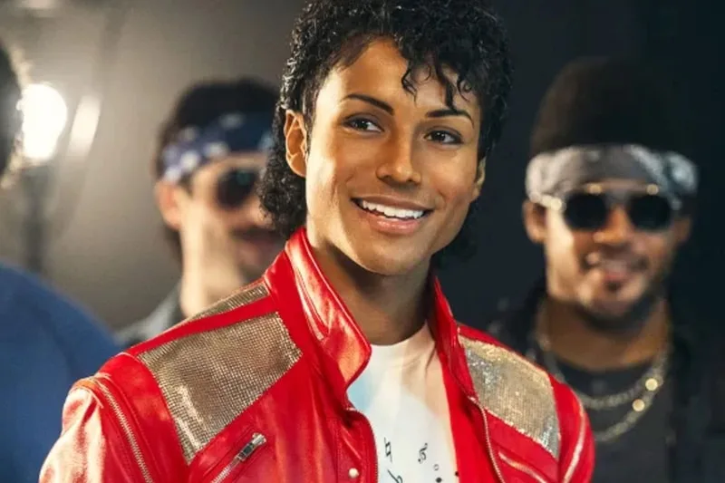 Personne souriante en veste rouge brillante, cheveux bouclés noirs.