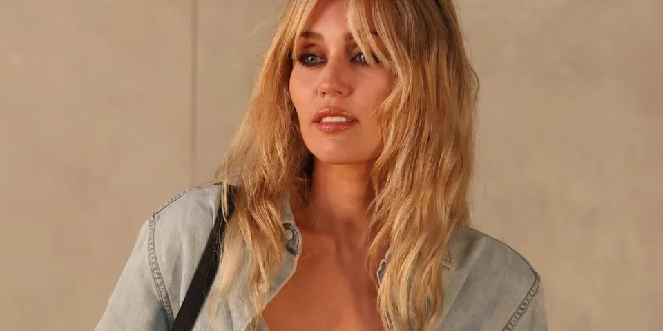 Femme blonde en chemise en jean avec maquillage intense.