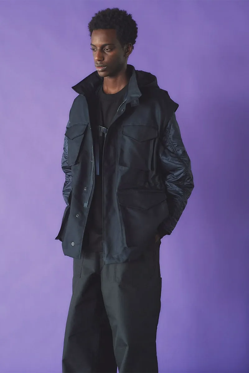 Homme posant dans une veste noire sur fond violet.