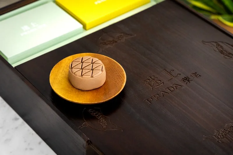 Pâtisserie sur assiette dorée, boite de luxe avec logo Prada.
