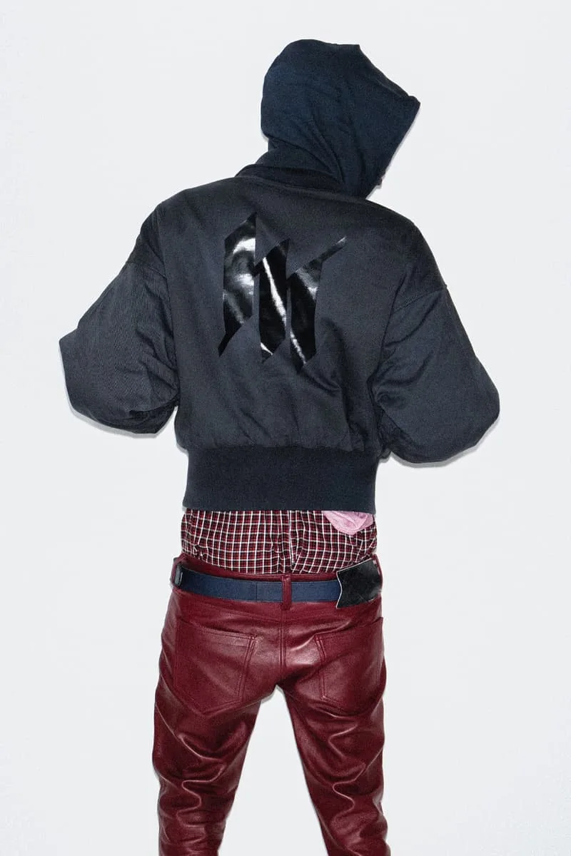 Personne en veste noire avec logo, pantalon rouge, capuche.