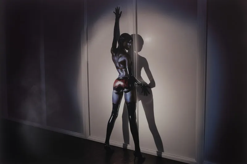 Personne en tenue brillante posant contre un mur, effet dramatique d'éclairage et d'ombre.