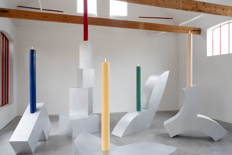 Installation artistique avec bougies colorées et structures métalliques abstraites.