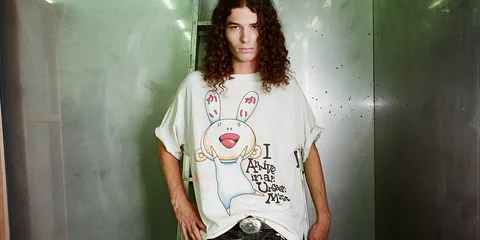 Homme aux cheveux longs portant un t-shirt graphié décontracté.